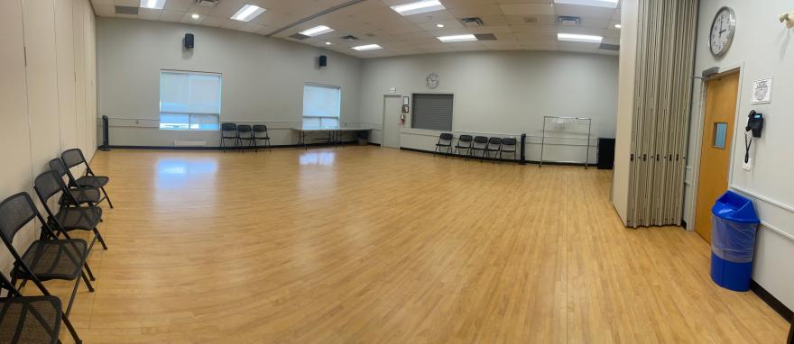 Spacious dance studio with wooden floors and chairs against the walls.