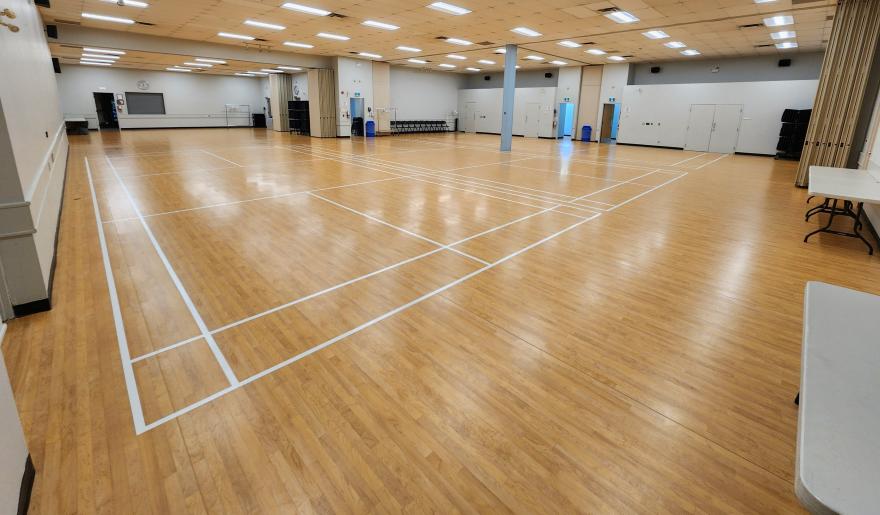 Spacious gym with a wooden floor and white court lines.