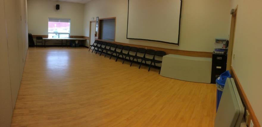 Empty meeting room with rows of chairs, projector screen, and wooden floor.