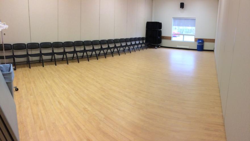 Empty conference room with wooden floor and rows of chairs against the wall.