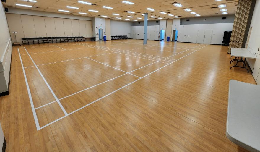 Empty gymnasium with wood flooring and white court lines.