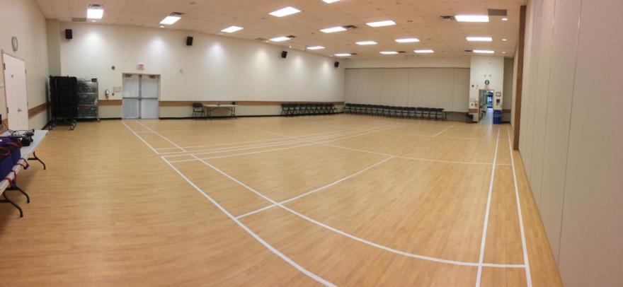 Spacious indoor gym with wooden floor, white lines, and overhead lights.