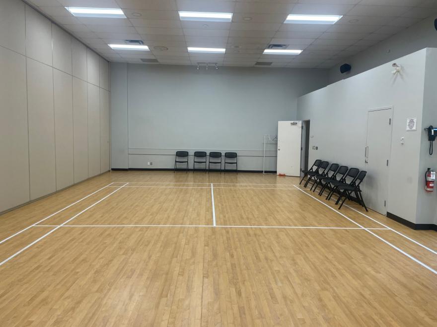 Empty gym room with wooden floor and stacked chairs.