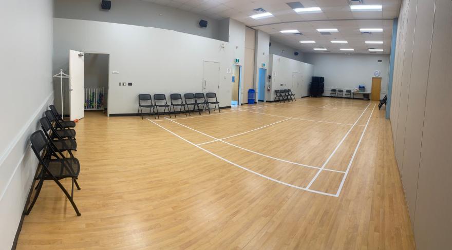 Spacious indoor gym with wooden floor, lined chairs, and overhead lights.