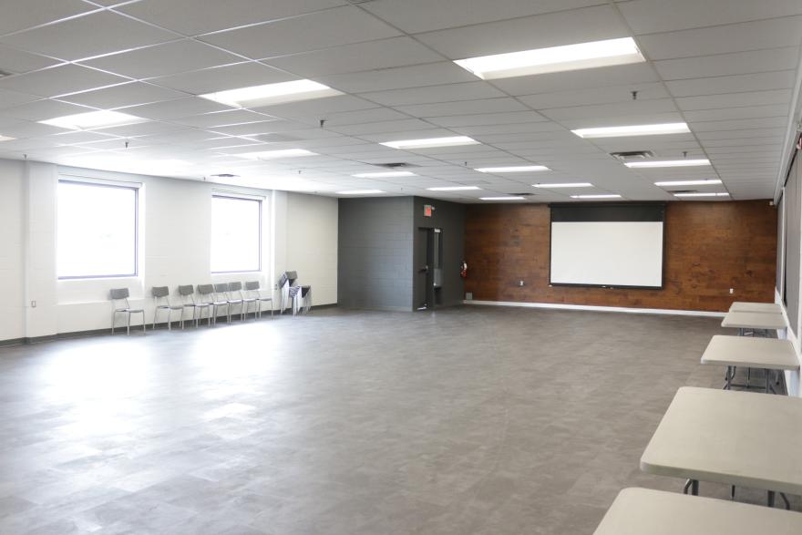 Spacious empty room with chairs, tables, and a projector screen.