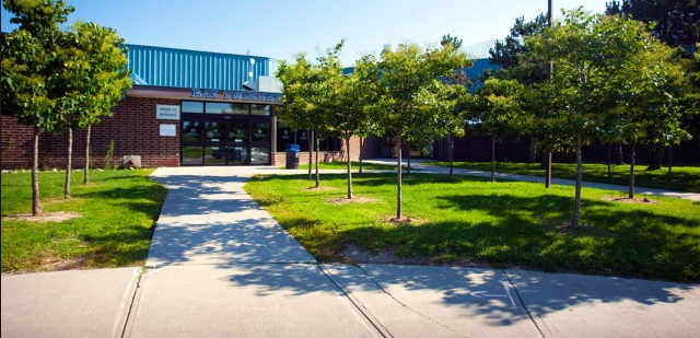 School entrance with blue roof, surrounded by trees and a walkway.